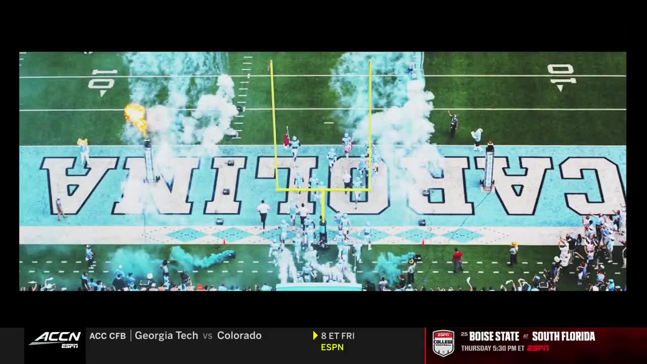 The team in white uniforms is running onto the field, emerging from a cloud of white and blue smoke.  They're heading toward the goalposts as the crowd cheers.
