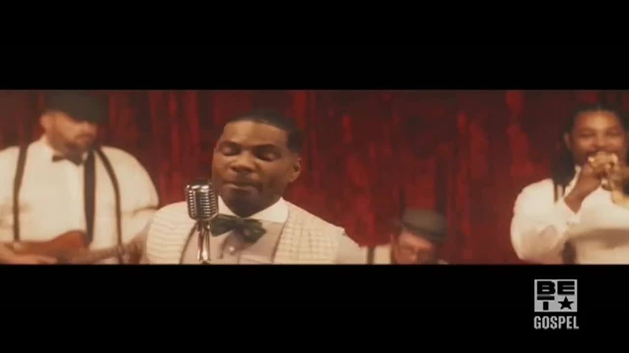 A man in a bow tie sings into a vintage microphone, backed by a band in a dimly lit room. The BET Gospel logo is visible in the corner.
