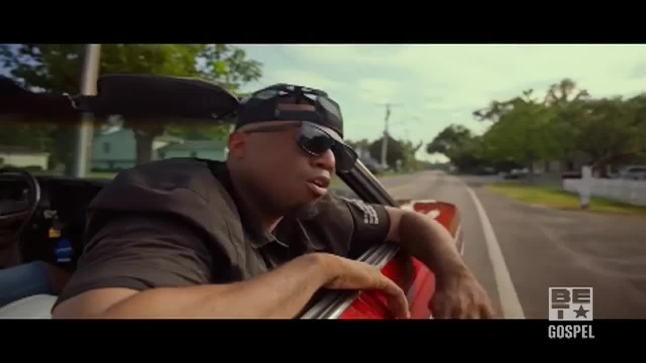 A man in sunglasses leans out of a red convertible, driving down a tree-lined road. The BET Gospel logo sits in the corner, suggesting this is a music video.
