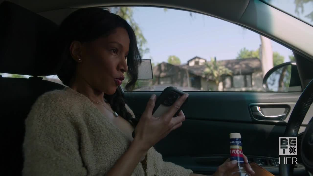 A woman in a car, holding a phone, looks intently at the screen while a bottle of vodka rests in her lap. The scene, set in the United States, is branded with the BET Her logo.
