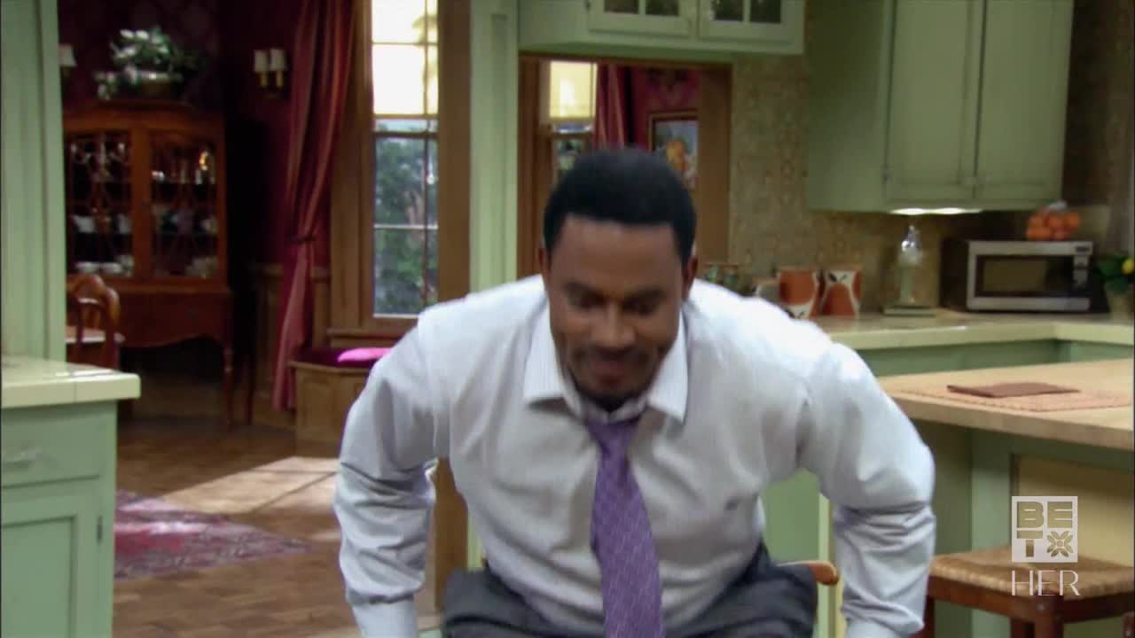 A man in a white shirt and purple tie bends forward, his gaze fixed downwards. He's in a kitchen, and the BET Her logo is visible in the corner.

