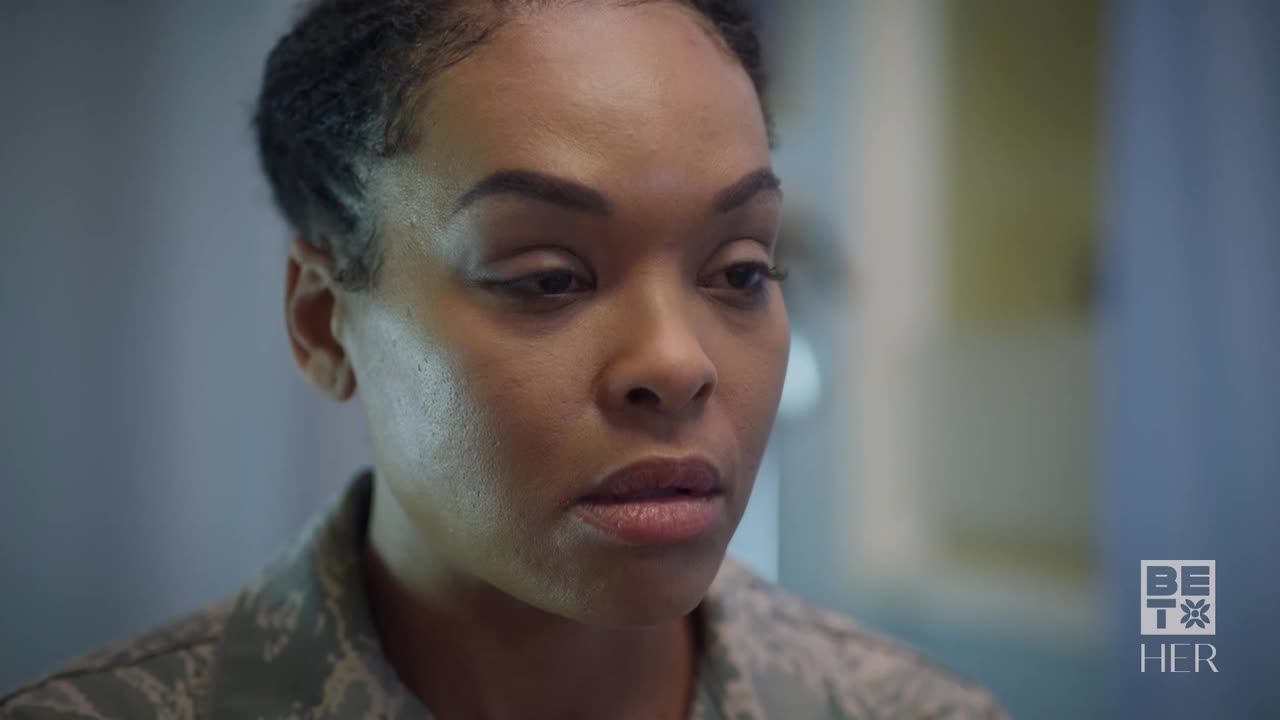 Her gaze is fixed, her lips slightly parted as if she's about to speak. The BET Her logo is visible, and she's wearing a military-style uniform.
