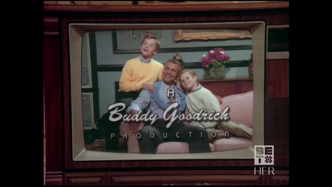 A vintage television screen displays a family of three, seated on a pink couch. The "Buddy Goodrich Production" logo is centered below the image, with the BET Her logo in the corner.
