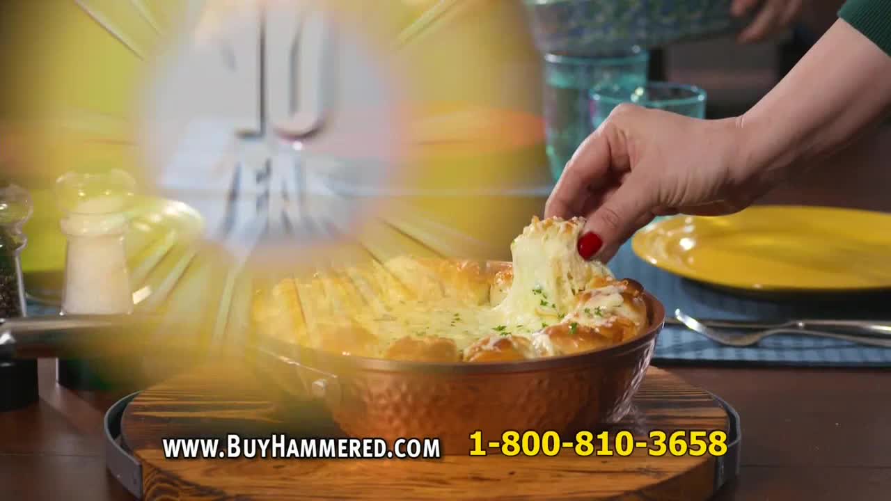 A hand with red nail polish pulls a cheesy bread bite from a copper-colored dish. The cheese stretches, and the bread looks golden brown.
