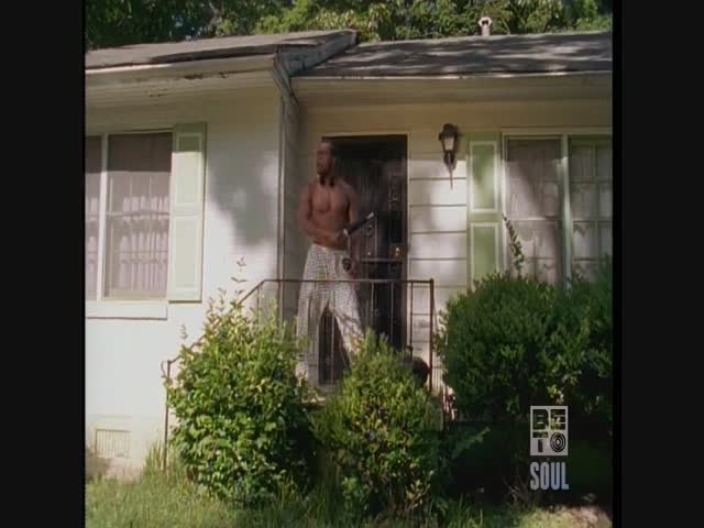 A shirtless man stands on the porch, holding a weapon. He's in front of a small house, the BET Soul logo visible in the corner.
