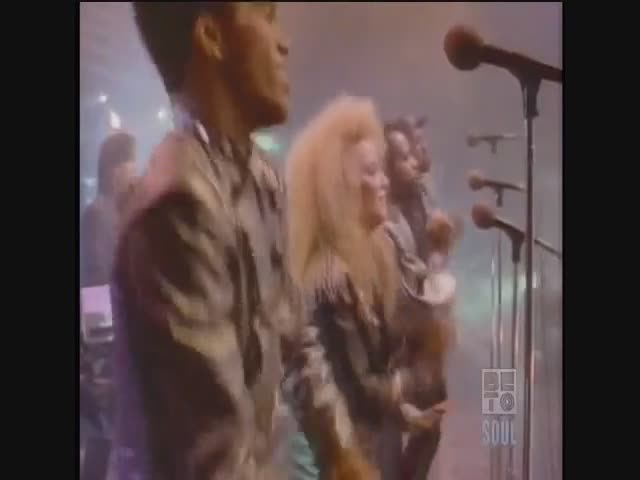 A band, bathed in stage lights, is performing on BET Soul. The lead singer with big blonde hair is belting into a microphone while the others sway and play their instruments.
