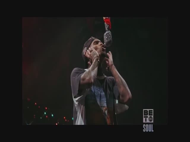 The singer is mid-song, head tilted back, eyes closed, and hands framing his face. A microphone hangs from above, and the BET Soul logo is visible in the corner.
