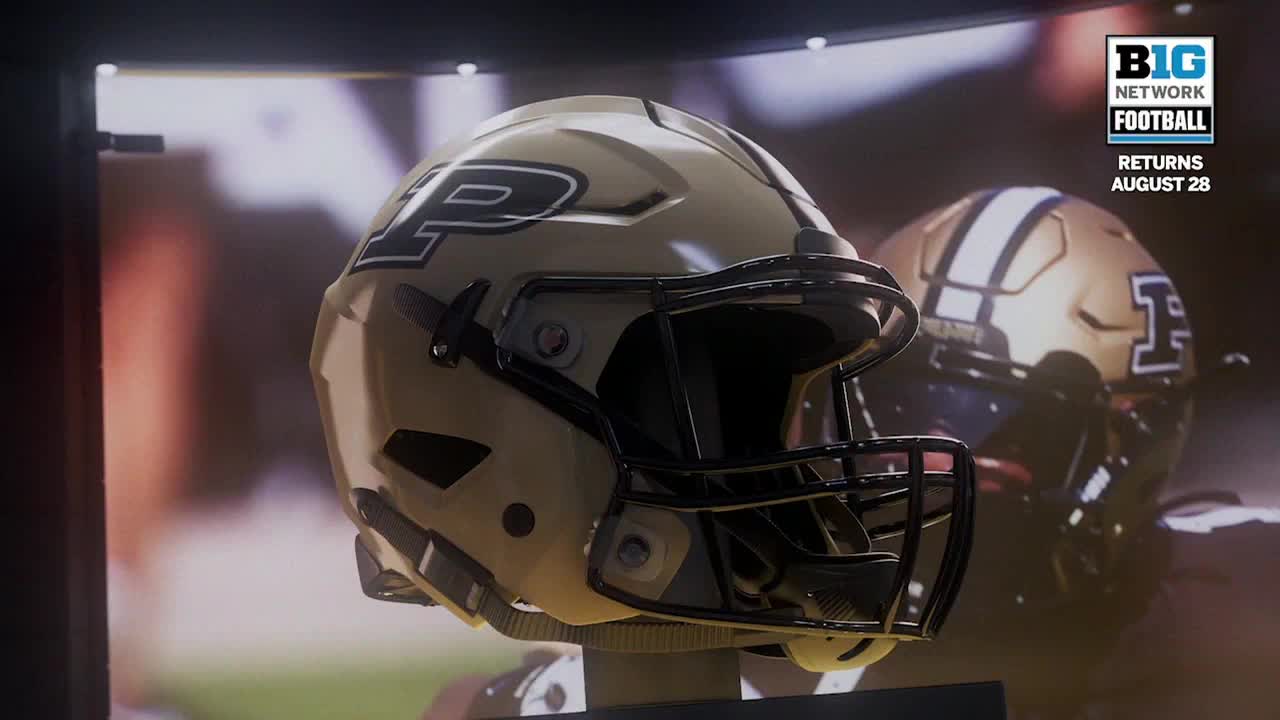 A Purdue Boilermakers helmet, gleaming gold, is displayed in a glass case. The Big Ten Network logo and a return date are visible in the background.
