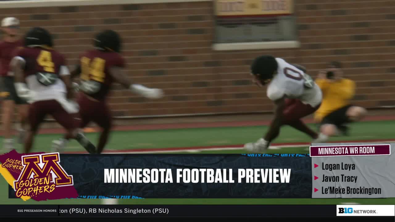 Two players in maroon jerseys sprint downfield, while another, in white, dives toward the end zone. A photographer kneels nearby, capturing the action for the Big Ten Network.
