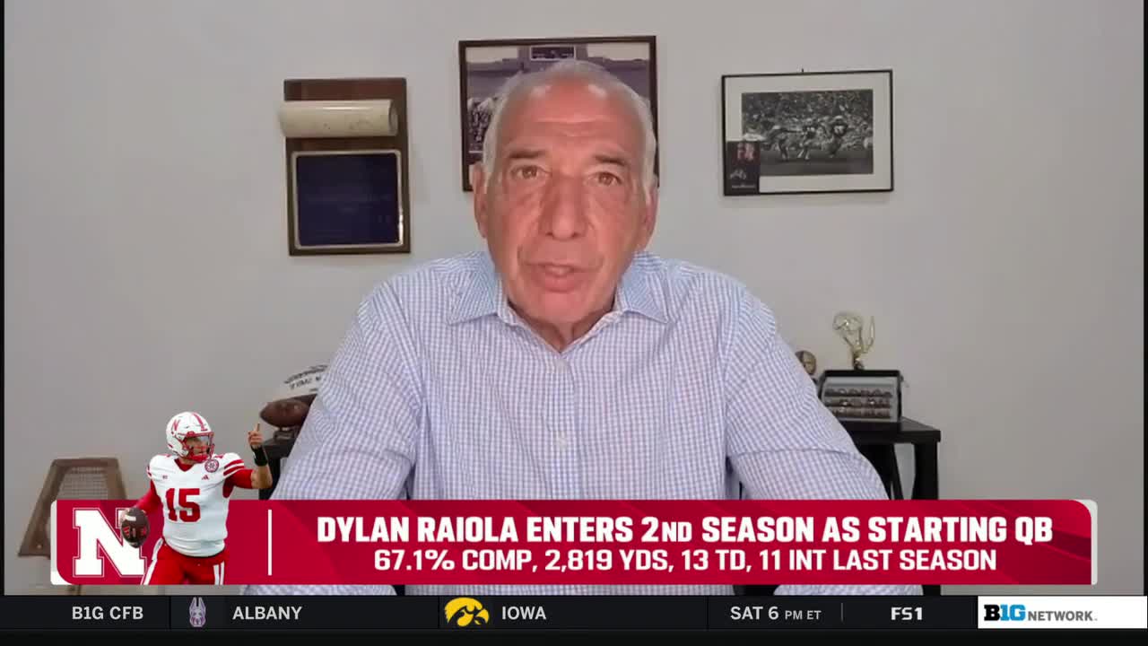 A man in a blue-and-white striped shirt is speaking directly to the camera. Below him, a graphic on the Big Ten Network displays stats about a quarterback named Dylan Raiola.
