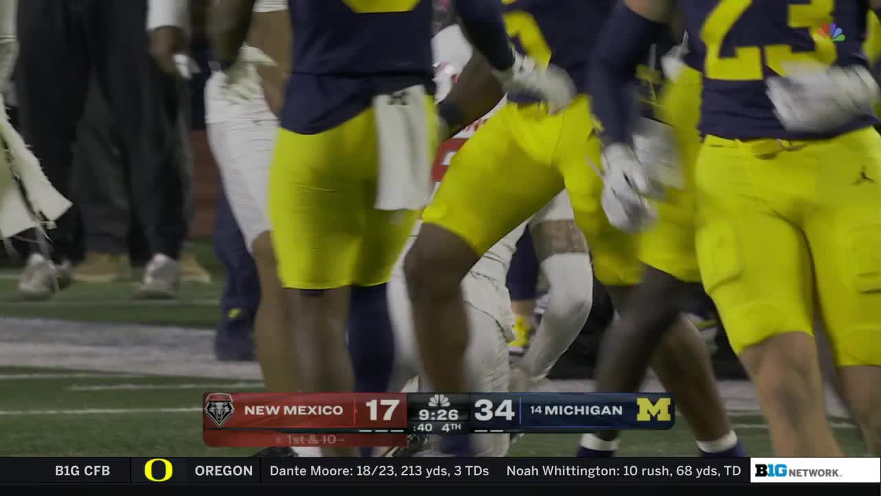 Players in maize and blue are clustered together, their legs pumping as they move toward the right. The scoreboard on the Big Ten Network shows Michigan with a lead over New Mexico in the fourth quarter.
