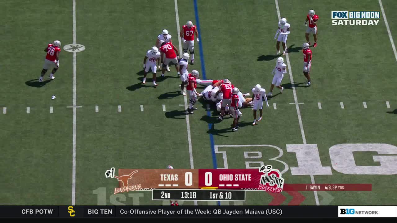 A pile of red and white jerseys is huddled near the center of the field. Players in white uniforms stand around the group, while others move away.
