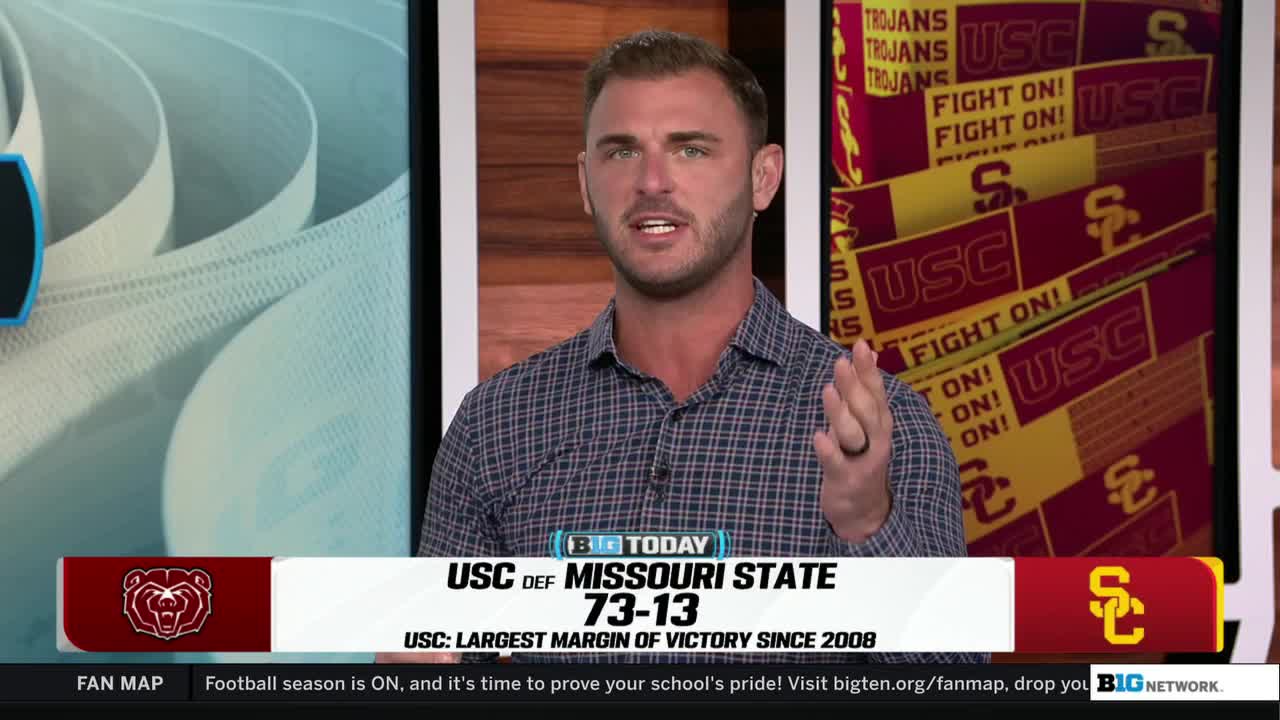 The man in the checkered shirt is talking, gesturing with his right hand. Behind him, a graphic displays the USC victory over Missouri State on the Big Ten Network.
