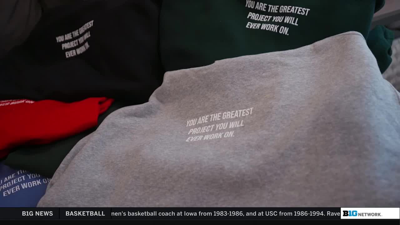 Several sweatshirts in different colors are stacked, each bearing the same white text on the back. The gray one in the foreground has the phrase "You are the greatest project you will ever work on" printed on it.
