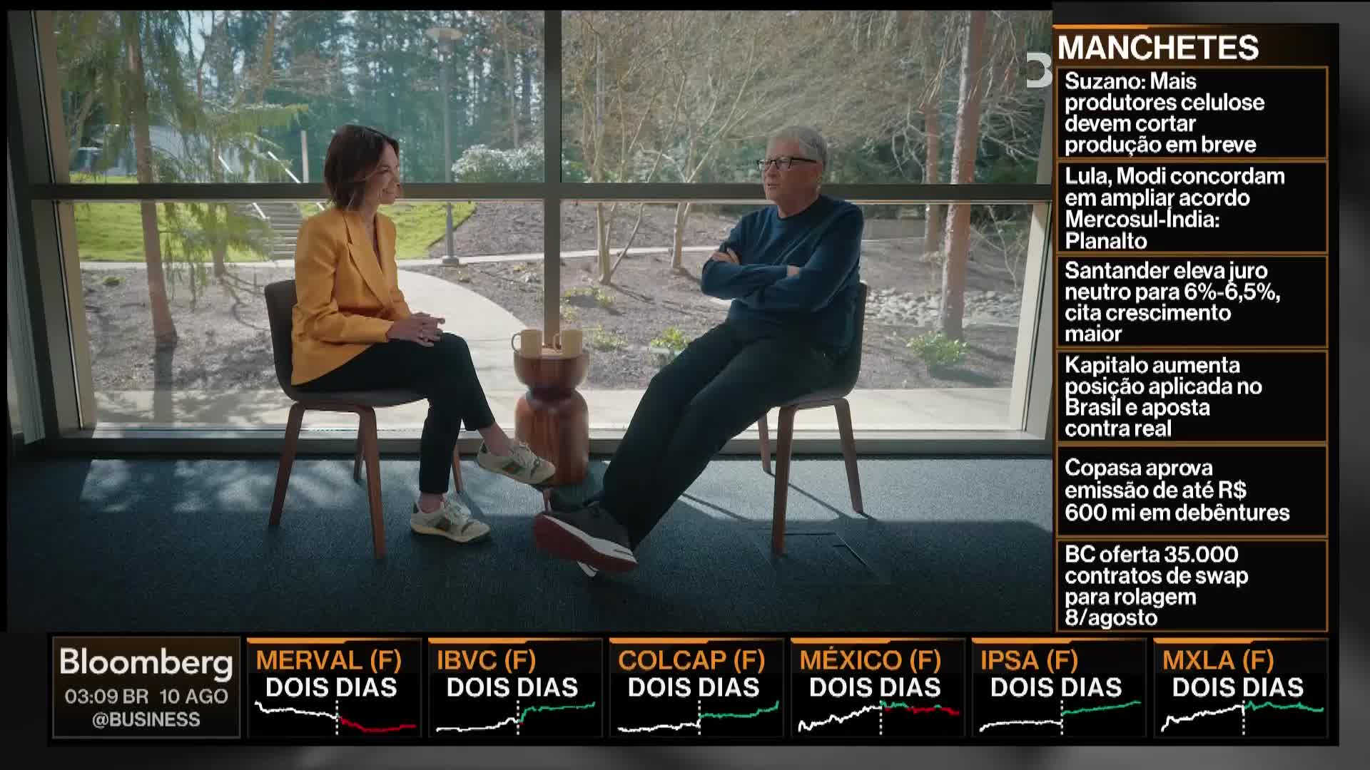 A woman in a yellow blazer sits across from a man in a blue sweater, both in chairs, with a large window behind them. The Bloomberg TV logo is visible in the corner, and the news ticker is running on the right.
