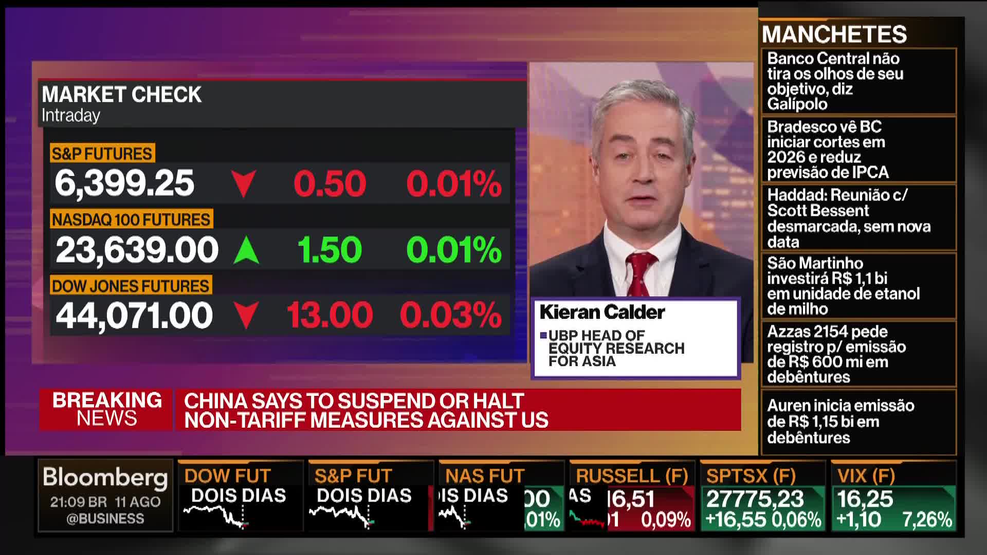 On Bloomberg TV, a man in a suit is speaking, while stock market numbers flash on a screen to his left. Headlines in Portuguese scroll on the right, and a ticker at the bottom displays more financial data.
