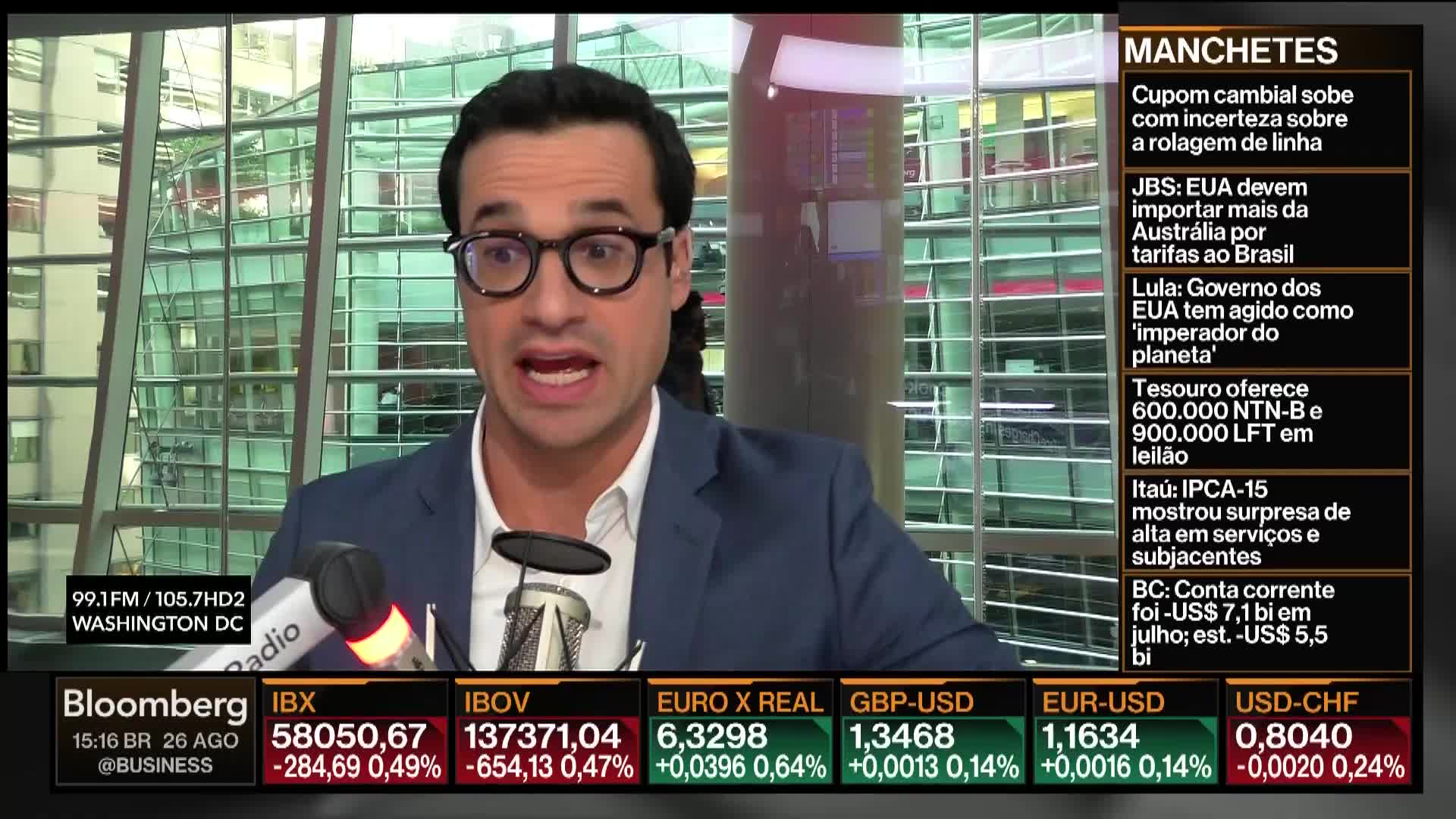 A man in a suit jacket, wearing glasses, is speaking into a microphone on a Bloomberg TV set. Financial data and news headlines are displayed on the screen behind him.
