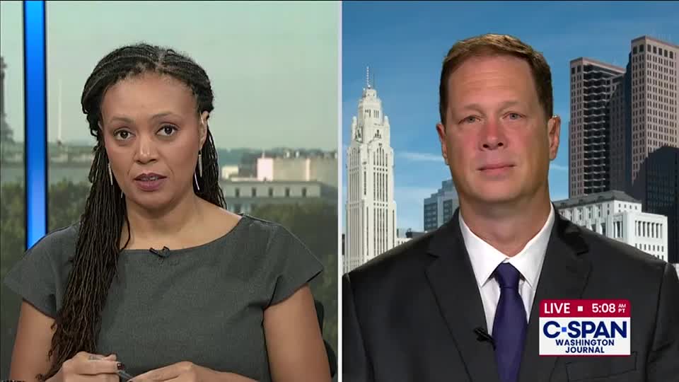A woman with long braids looks directly at the camera from a studio set. On the right, a man in a suit is framed against a cityscape, the C-SPAN logo visible in the corner.
