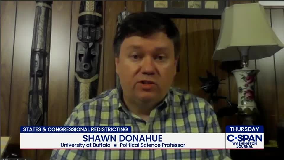 A man in a plaid shirt speaks, his face filling the screen on C-SPAN. The chyron identifies him as a political science professor discussing states and congressional redistricting.
