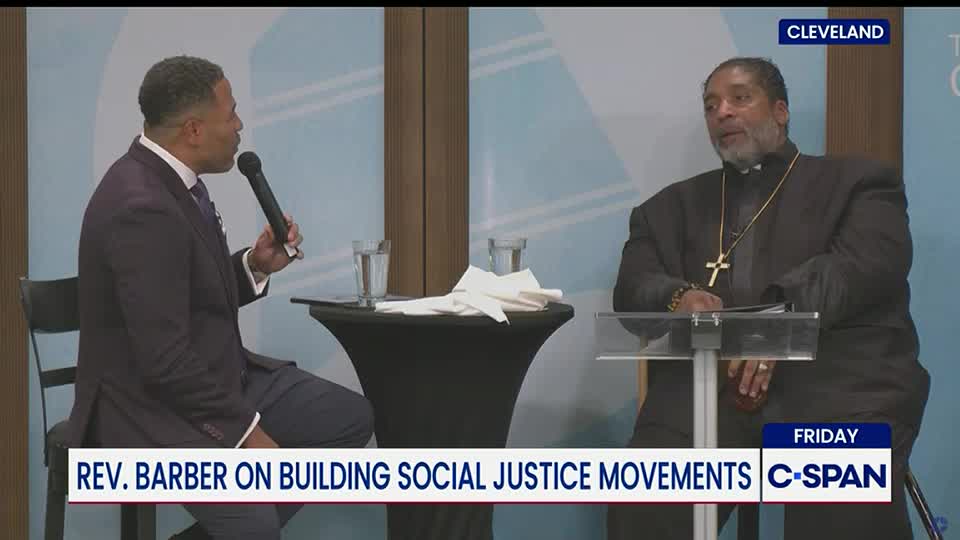 The man in the suit holds a microphone, gesturing as he speaks to the man in the clerical collar. The C-SPAN logo is visible at the bottom of the screen, indicating the event is being broadcast from Cleveland.

