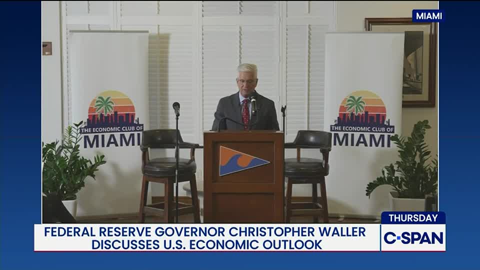 A man in a suit stands behind a podium, speaking into a microphone. The backdrop features banners for the Economic Club of Miami, as seen on C-SPAN.
