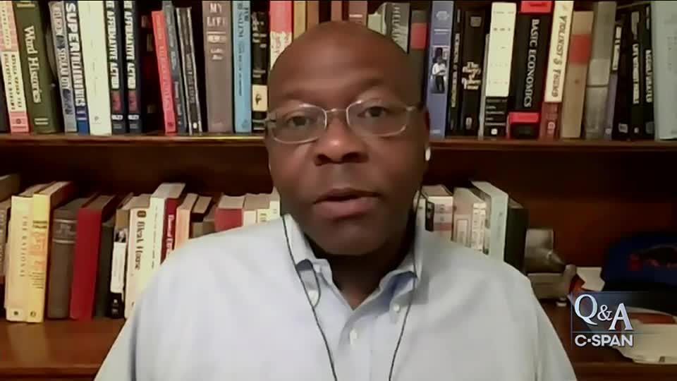 A man wearing glasses and a light blue shirt speaks directly into the camera, with a bookshelf full of books behind him. The C-SPAN "Q&A" logo is visible in the bottom right corner.
