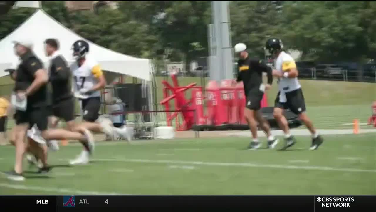 Players in black and white jerseys sprint across the green field, with a white tent and red training equipment in the background. The CBS Sports Network USA logo is visible in the corner.
