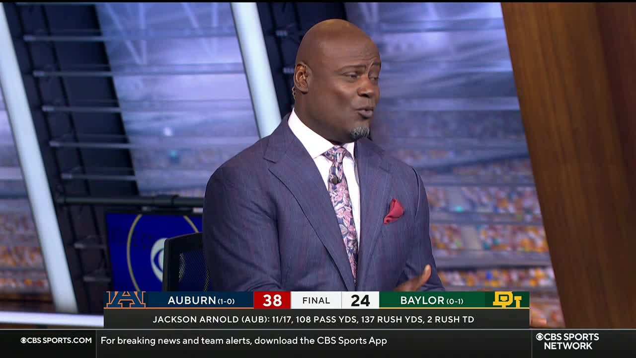 On CBS Sports Network USA, a man in a blue suit gestures while speaking. The score of a college football game between Auburn and Baylor is displayed below.
