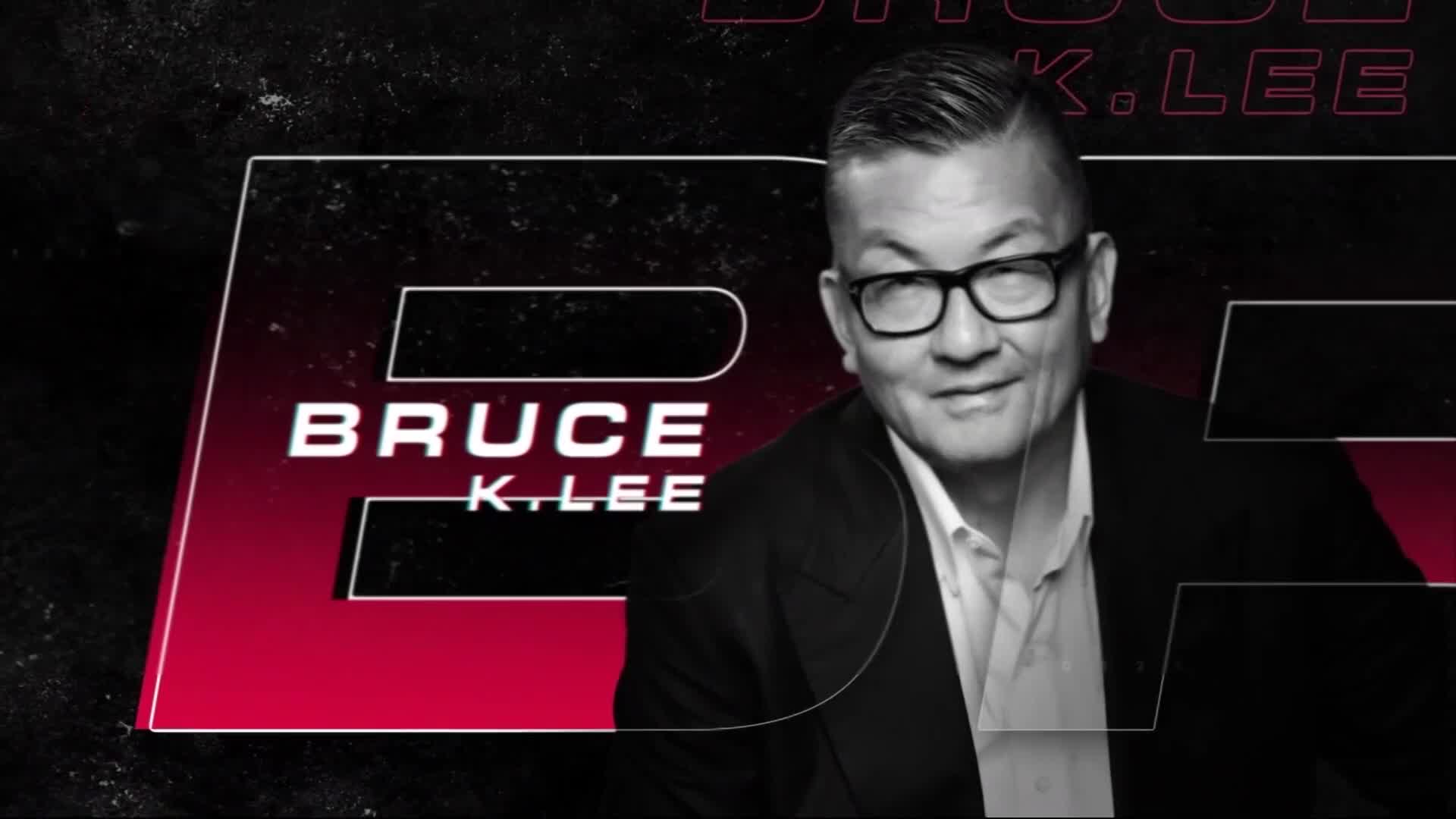 Bruce K. Lee, wearing glasses and a blazer, is smiling at the camera. His name is displayed in white letters over a red and black background.
