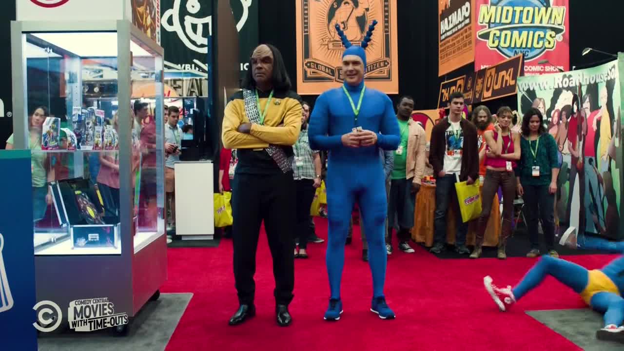 A man in a blue suit and antennae stands next to a Star Trek-uniformed figure, both posing on a red carpet. The Comedy Central logo is visible, and a costumed person is on the floor.
