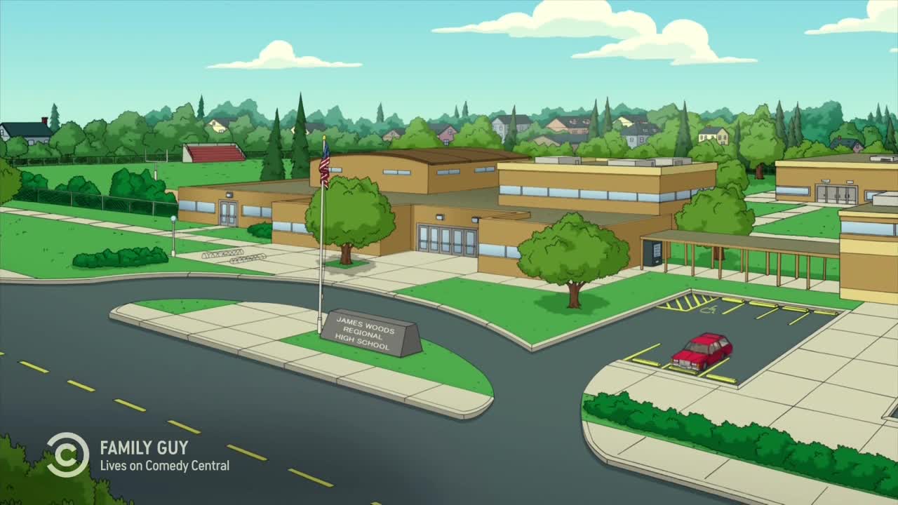 The James Woods Regional High School sits under a clear sky, the American flag waving gently in the breeze. A red car is parked in a handicap spot, and the Comedy Central logo is in the corner.
