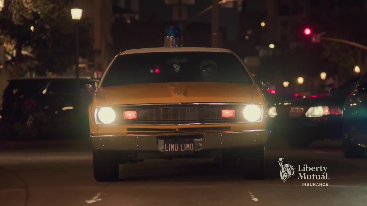 A yellow car, its headlights blazing, rolls toward me, the "LIMU LIMO" license plate clear. Other vehicles surround it on the street, and the night is lit by streetlights and traffic signals.
