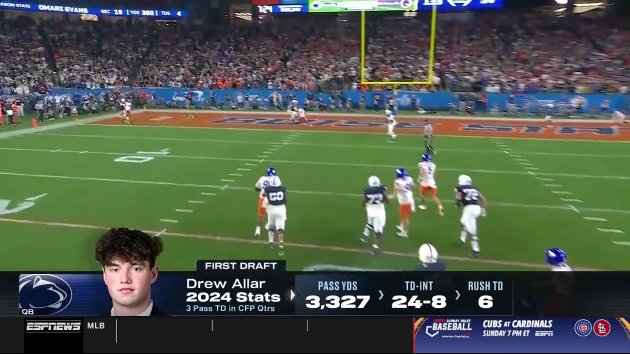 The receiver in white and blue is sprinting downfield, and a defender in orange is chasing him. The ball is already in the air, and the crowd in the stands is watching intently.
