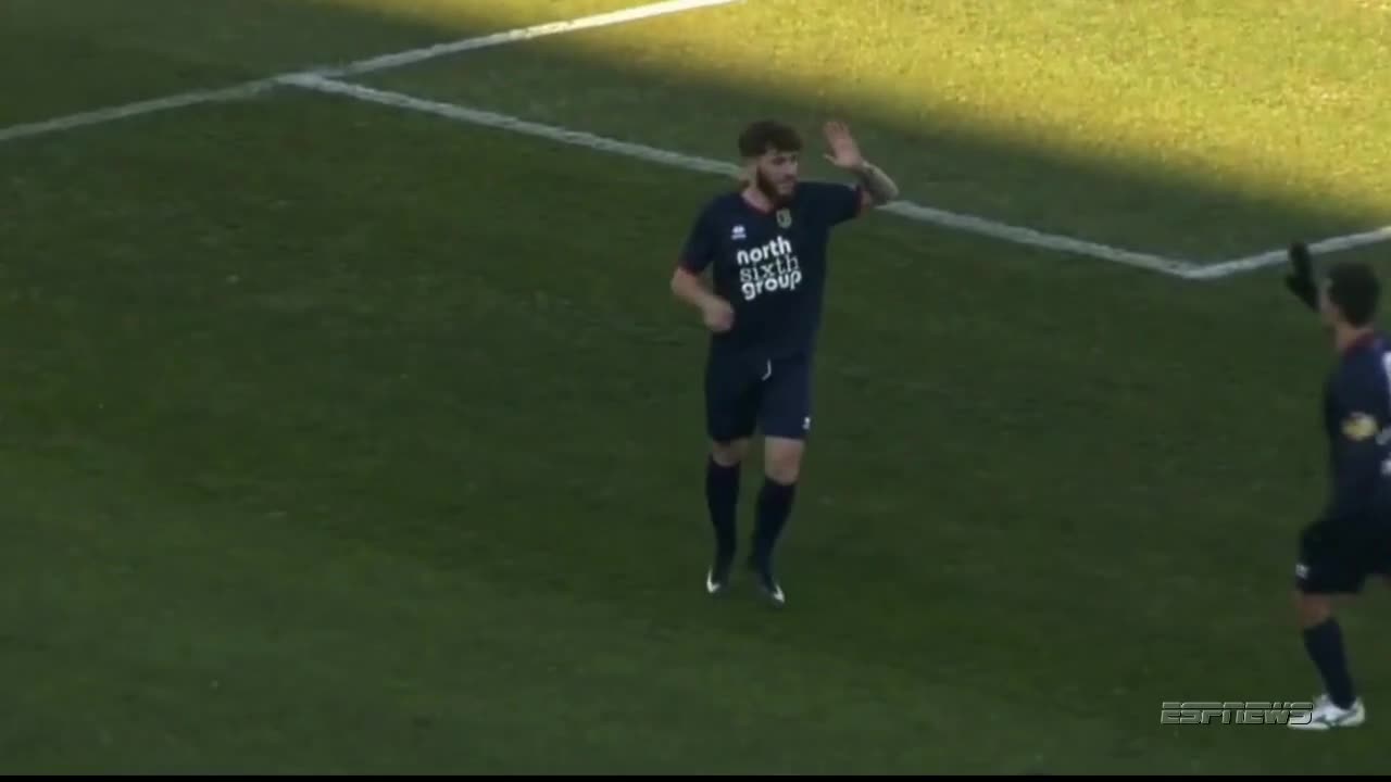 A player in a dark blue jersey jogs forward, waving his right hand in the air. Another player, also in dark blue, is already celebrating with his arm raised.
