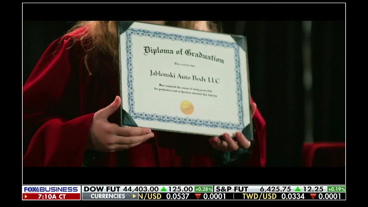 A person in a red graduation gown holds up a diploma, the text reading "Jablonski Auto Body LLC." The Fox Business Network logo and financial data are visible at the bottom of the screen.
