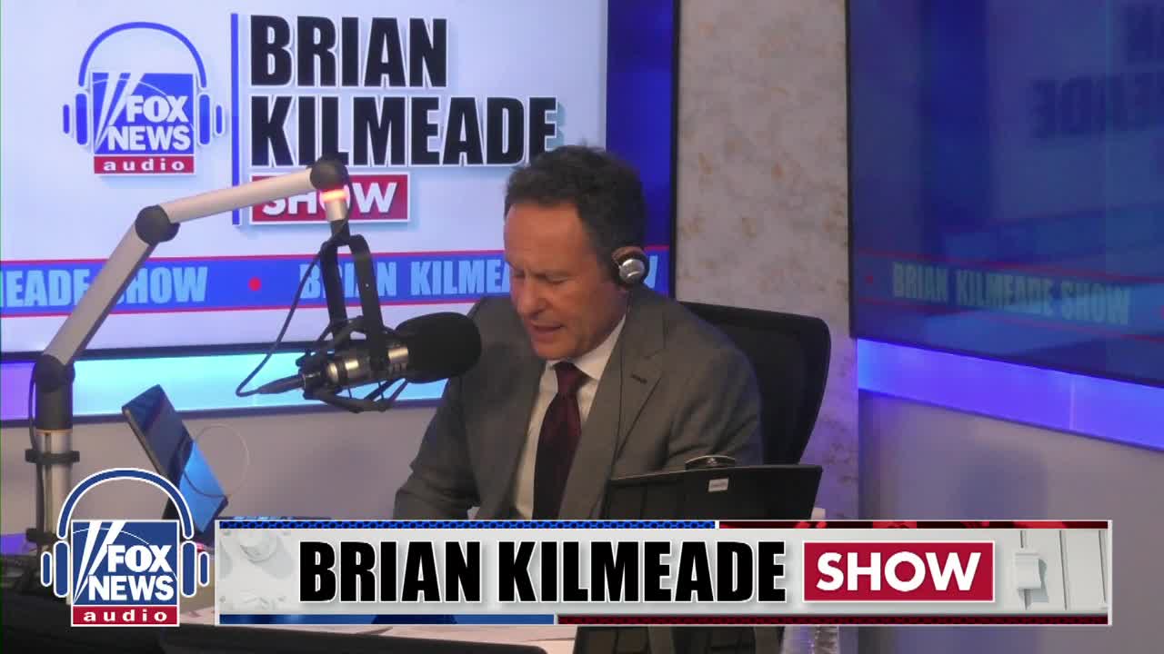 Brian Kilmeade is speaking into a microphone, wearing headphones. The "Fox News Audio" logo is visible on a screen behind him.