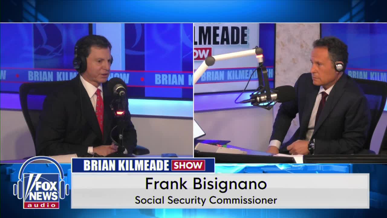 Two men sit at desks, each with a microphone in front of them. The man on the left wears headphones and a suit with a red tie, speaking into his mic. The man on the right, also in a suit and tie, looks intently at something off-camera. A graphic identifies the speaker on the left as Frank Bisignano, Social Security Commissioner, on the Brian Kilmeade Show.