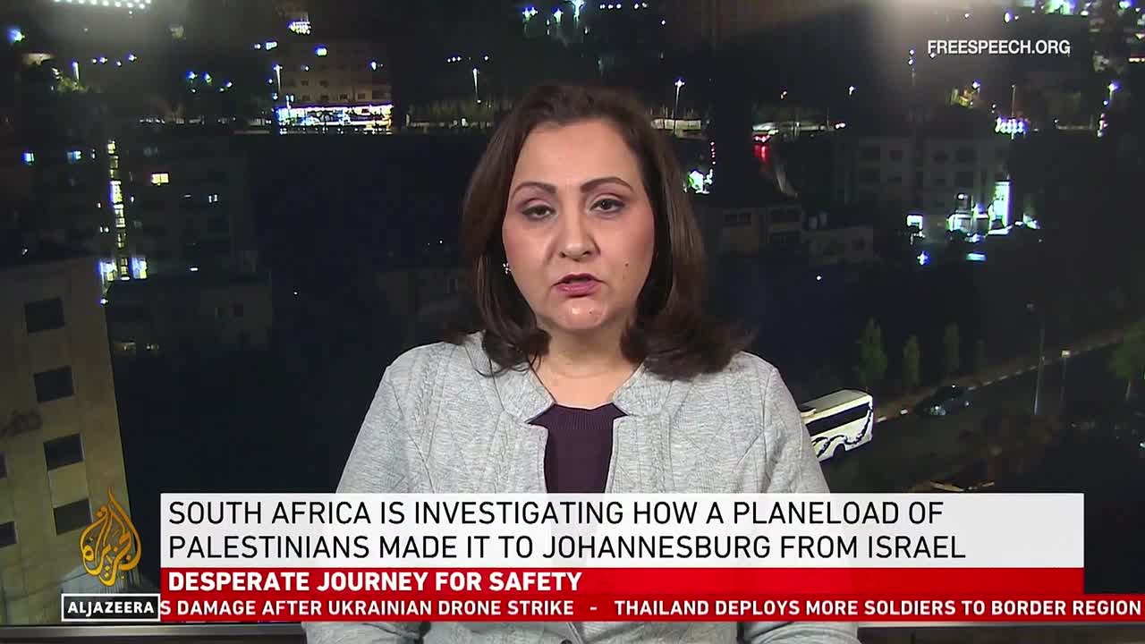 A woman in a gray sweater is speaking, framed against a nighttime cityscape visible through a window. The Free Speech TV logo is visible in the corner, and a news ticker below the speaker reads about South Africa and a flight of Palestinians.
