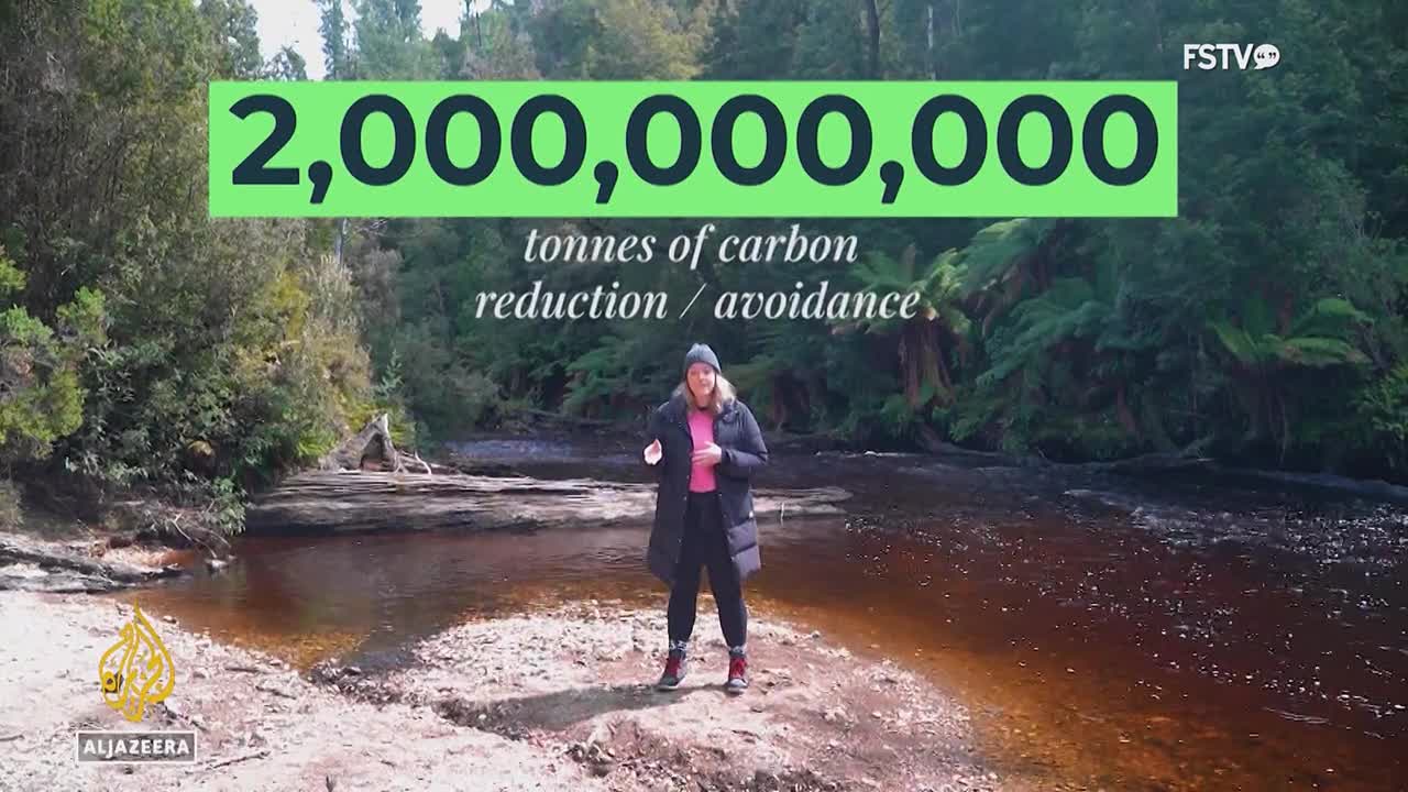 A woman stands in front of a river, speaking to the camera for Free Speech TV. Above her, a green box displays a large number, "2,000,000,000," and the words "tonnes of carbon reduction / avoidance."
