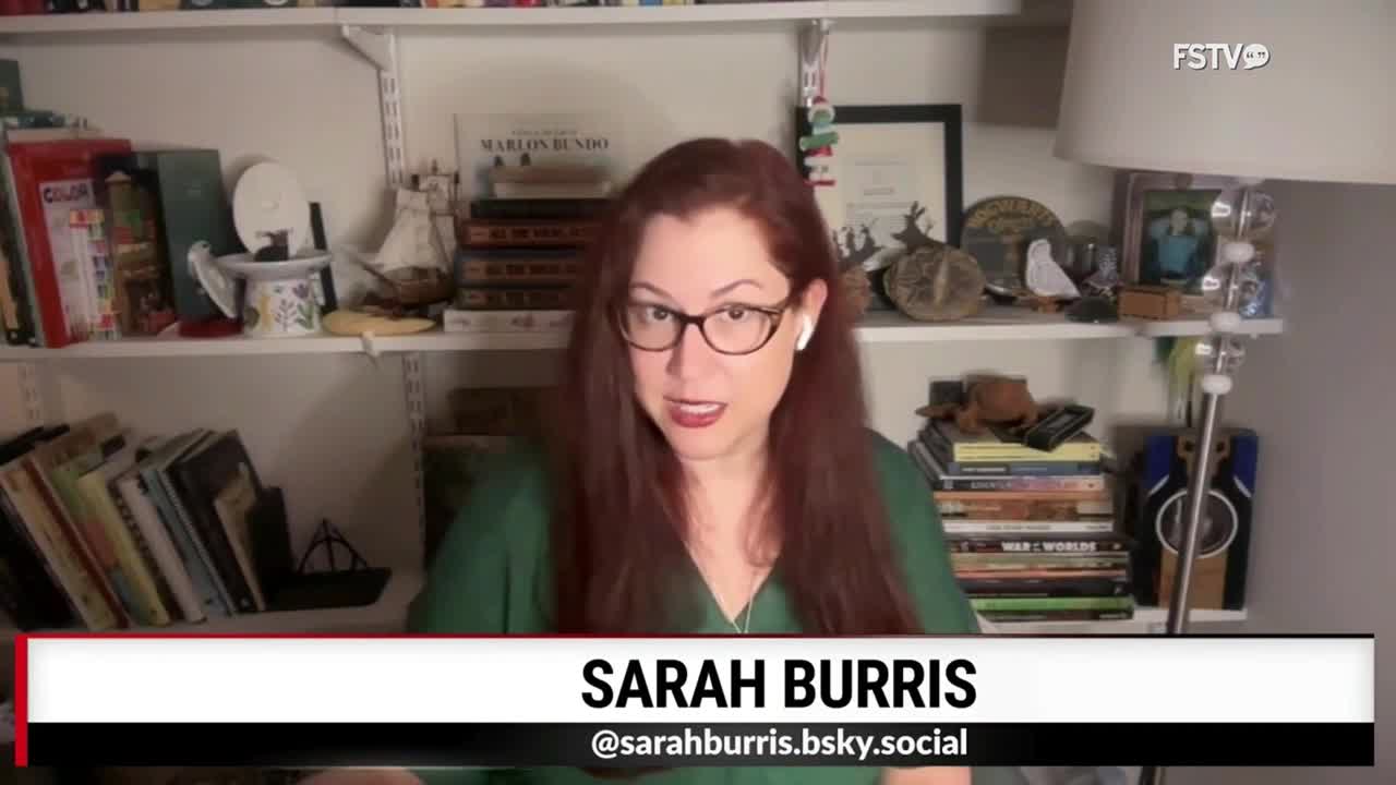 Sarah Burris, identified on Free Speech TV, is speaking directly into the camera. Bookshelves filled with items are visible behind her, and a lamp provides soft light to the right.
