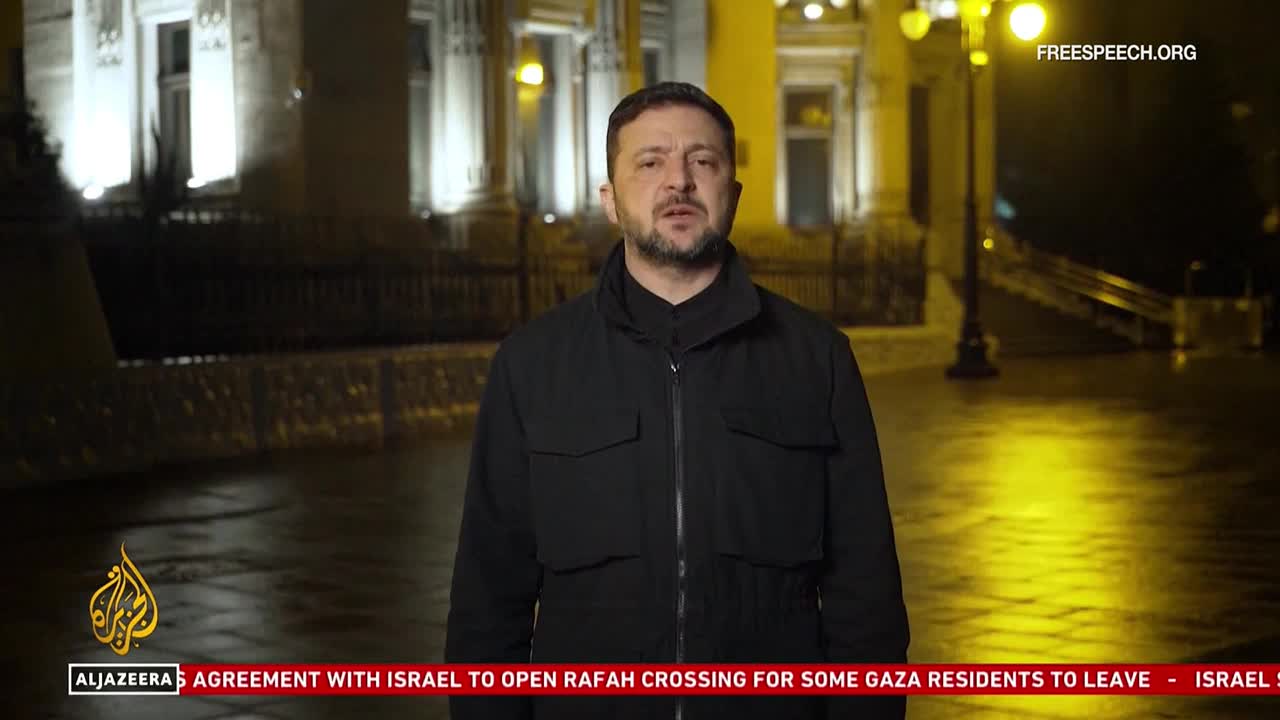 The man in the black jacket is speaking, framed by a dimly lit street and buildings. Below, a news ticker from Al Jazeera scrolls across the bottom of the screen.
