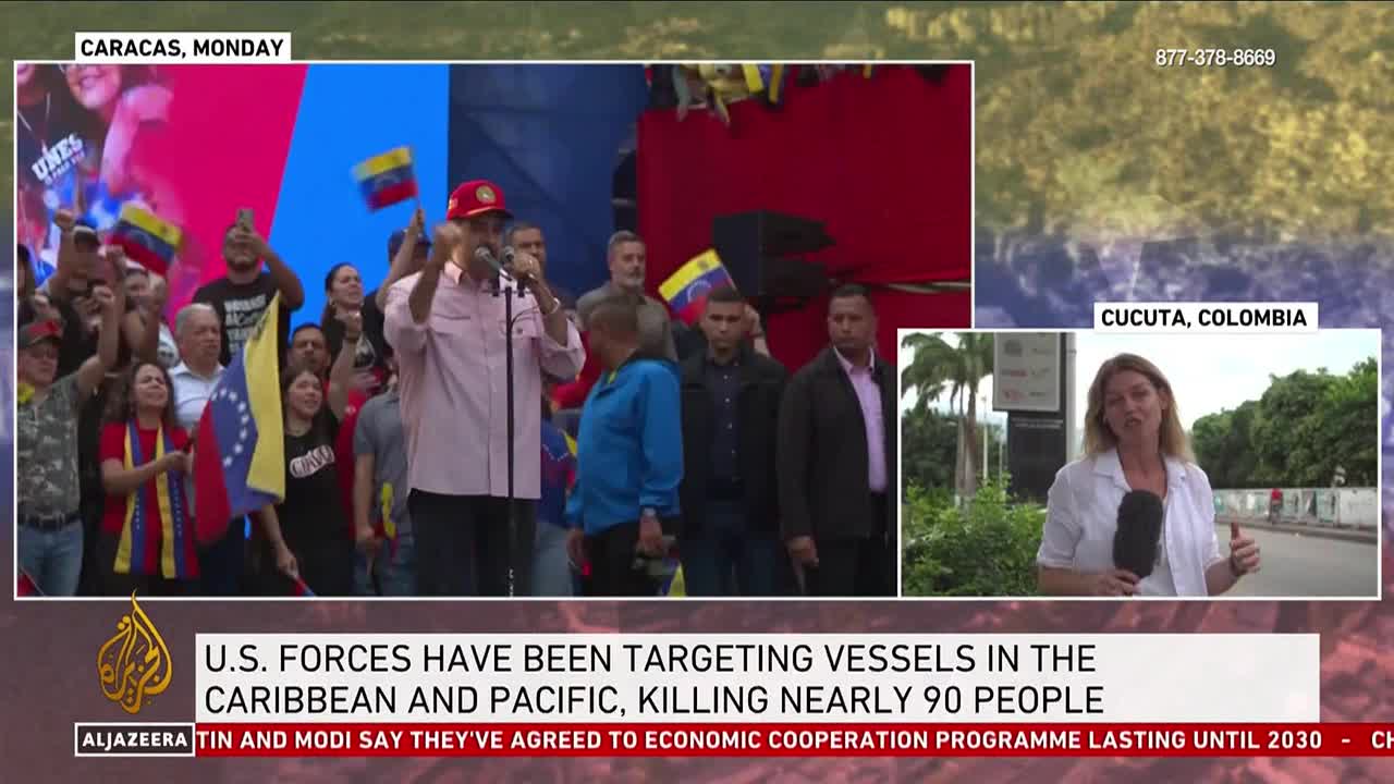 A man in a red cap speaks into a microphone, gesturing with his hands as a crowd waves Venezuelan flags. A news anchor in Cucuta, Colombia, reports on the side.

