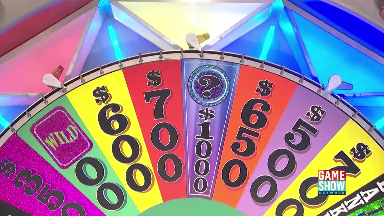 The colorful wheel is spinning on the Game Show Network, its white pointer about to land on a prize. The segments display dollar amounts and a "Wild" card, all in anticipation of the next contestant's turn.
