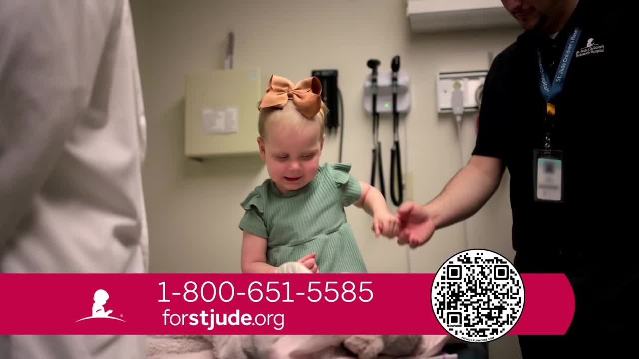 A small child, wearing a large bow, holds the hand of an adult while standing on an examination table. The child has a bandaged wrist and appears to be smiling.
