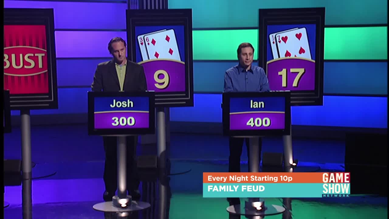 Two men stand at podiums, facing forward, with their scores and names displayed below. The Game Show Network logo is visible, advertising "Family Feud" starting at 10 p.m.
