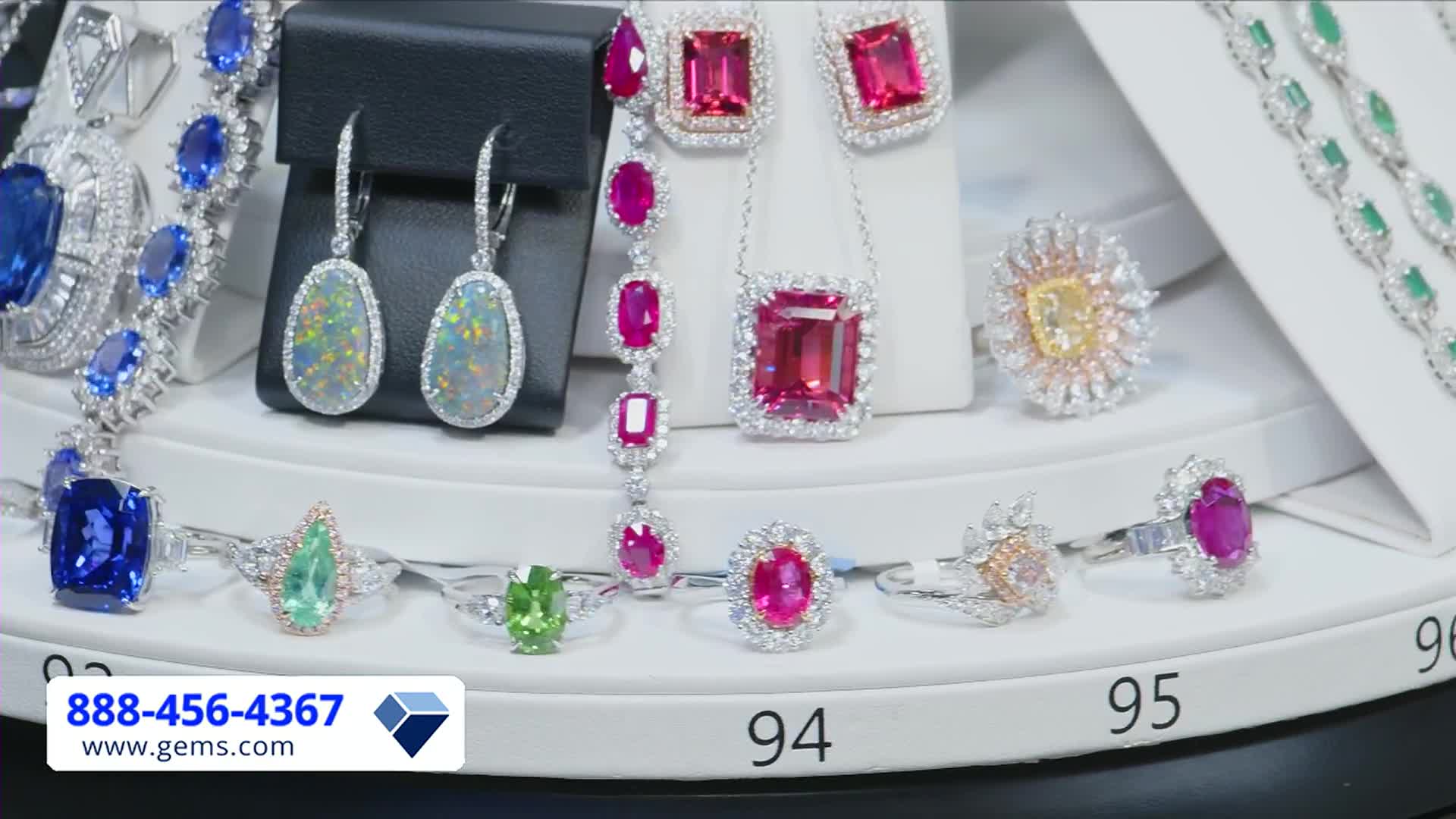 On a Gem Shopping Network set, a rotating display showcases various pieces of jewelry, including rings, earrings, and necklaces. The camera focuses on the sparkling gemstones, highlighting the intricate details and colors.
