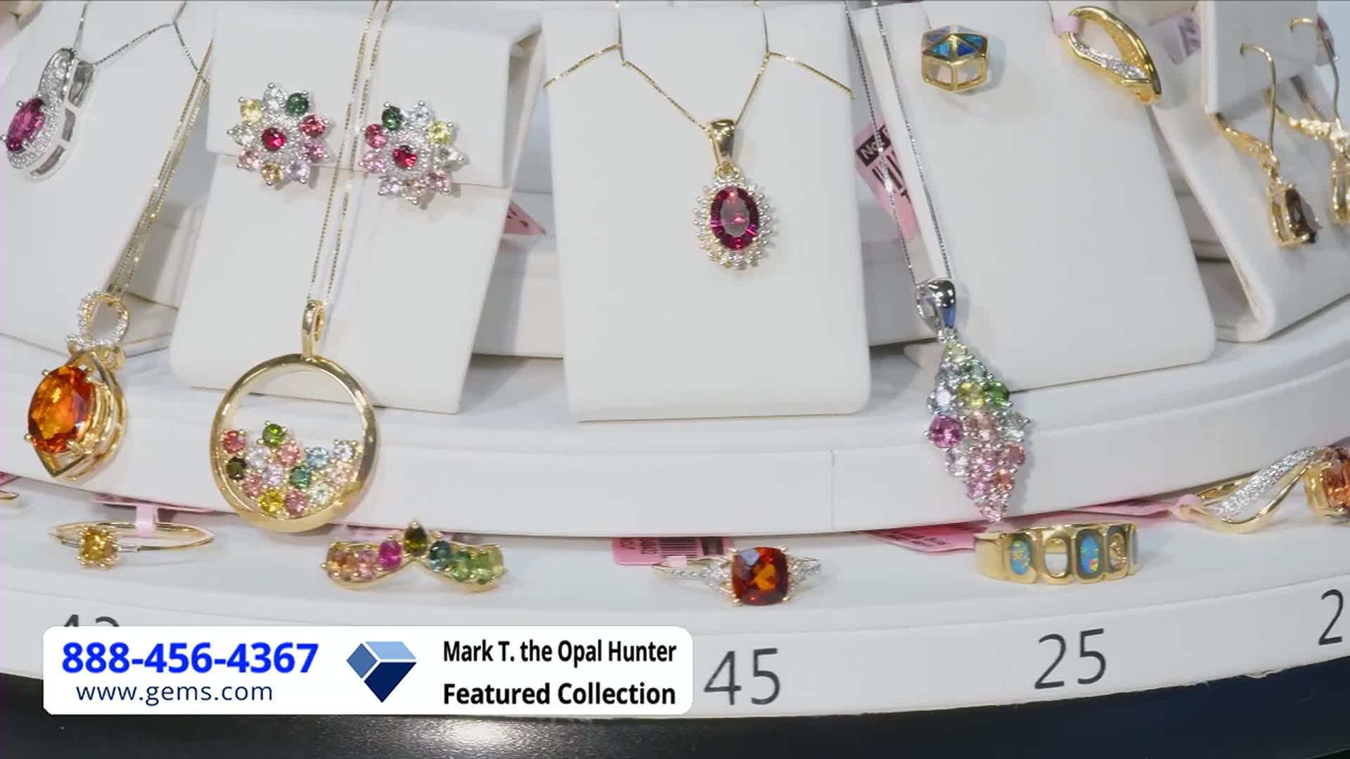 A rotating display showcases jewelry, each piece catching the light. The Gem Shopping Network's featured collection, including necklaces, rings, and earrings, is arranged on white pedestals.
