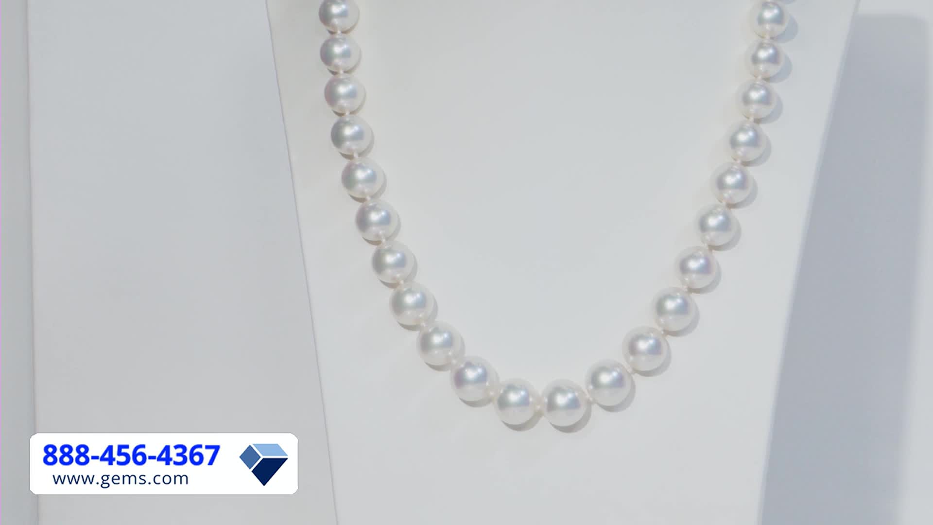 A strand of luminous pearls hangs on a white display, catching the light. The Gem Shopping Network logo and phone number are visible in the corner.
