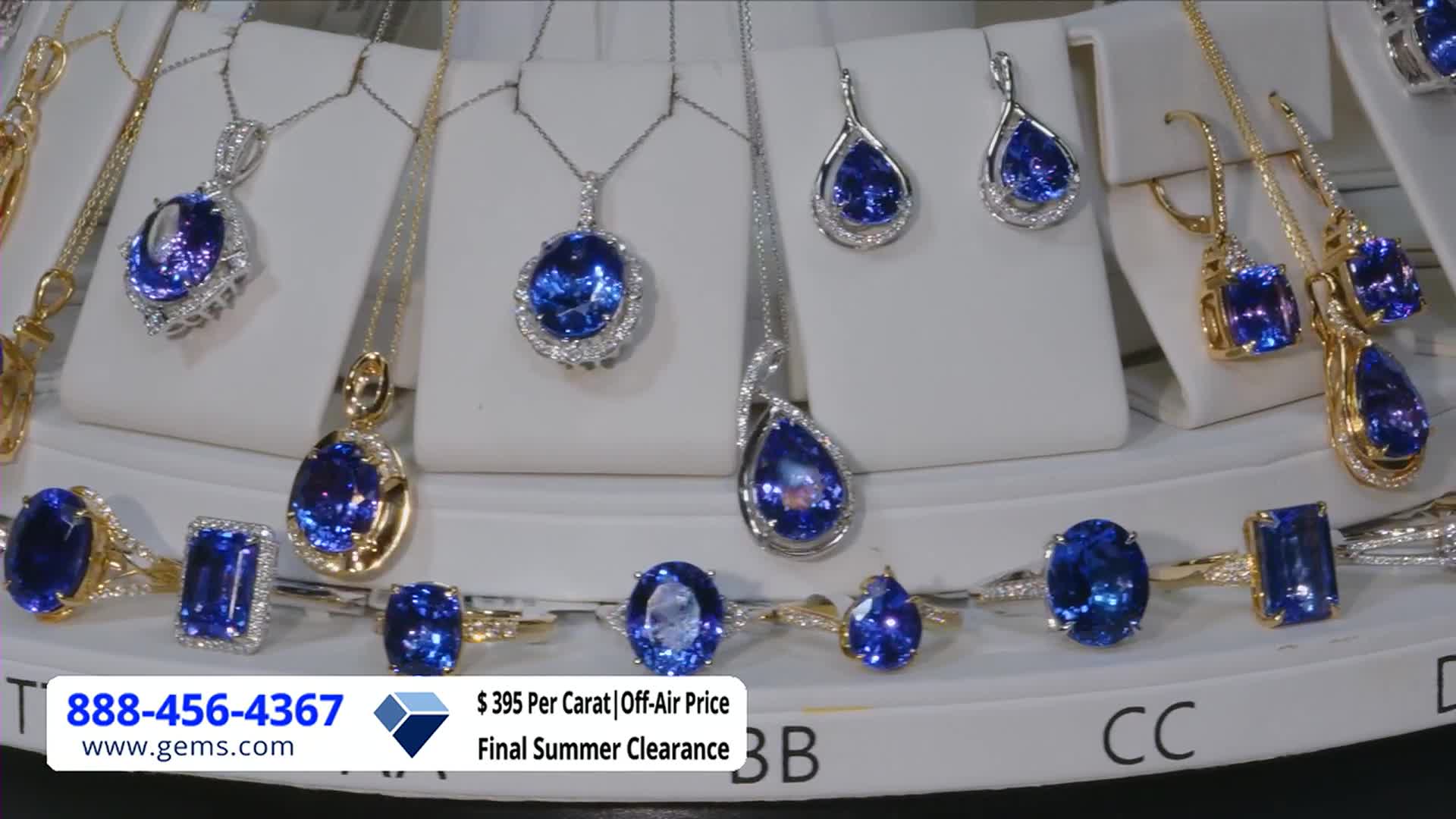 A display of jewelry, including necklaces, earrings, and rings, is arranged on a white surface. The Gem Shopping Network is advertising a final summer clearance with a phone number and website listed at the bottom.
