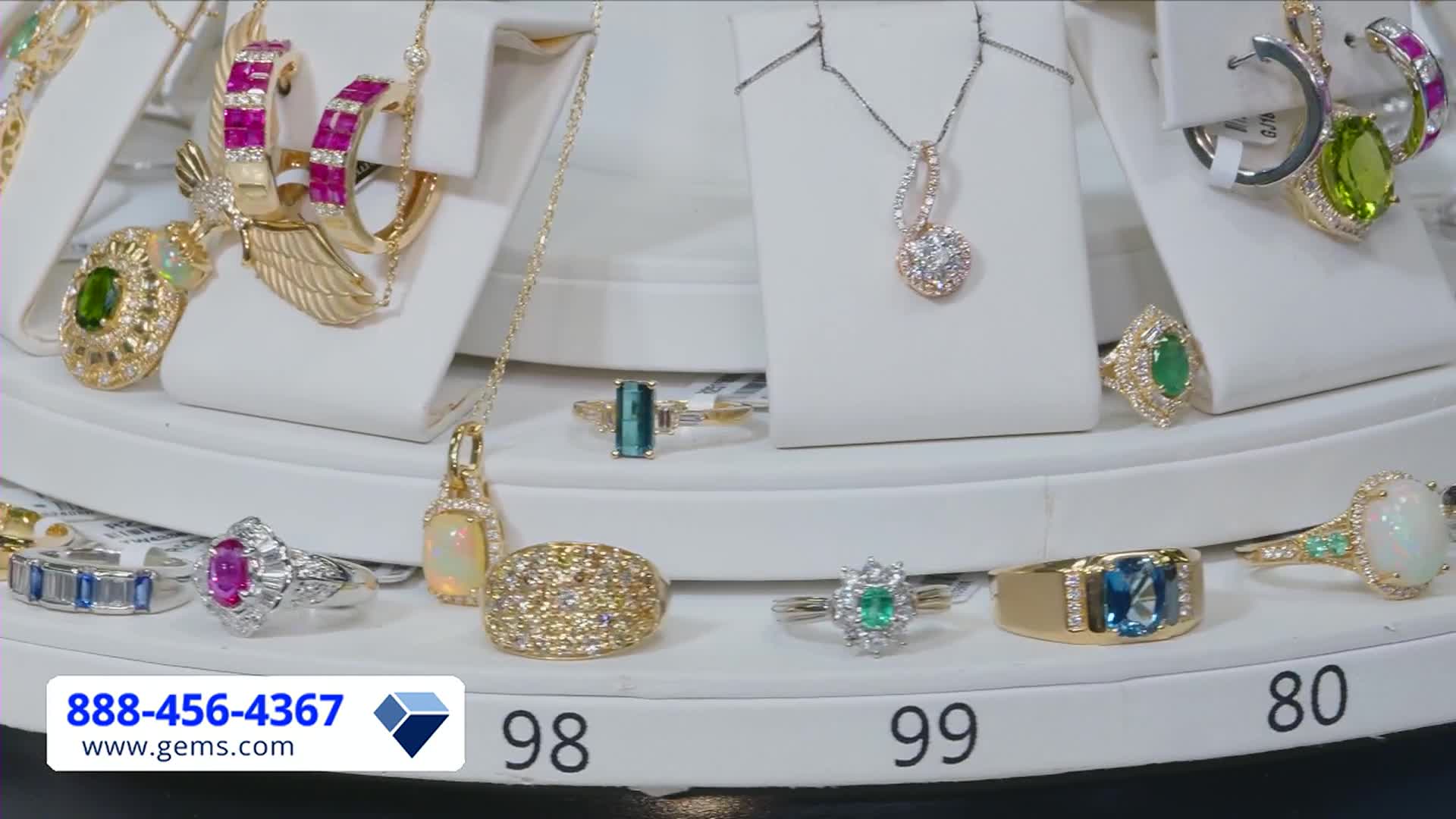 A rotating display presents jewelry, each piece sparkling under the lights. The Gem Shopping Network logo and phone number are visible at the bottom.
